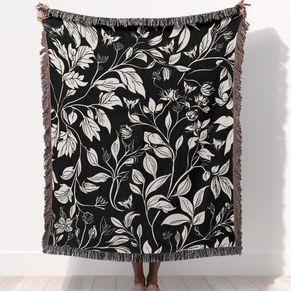 Person holding up a black and white floral woven tapestry blanket with moths design